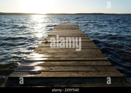 Wooden footbridge on lake and sun reflecting in water at sunset Stock Photo