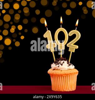 Birthday candle with cupcake - Number 102 on black background with out of focus lights Stock Photo