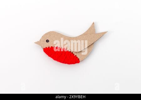 Simple craft representation of a bird made from cut-out pieces of material on plain white background. Brown cardboard body, red circular belly, black Stock Photo