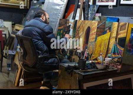 A man in a black jacket painting a cityscape during the Lok Mela festival in Islamabad, Pakistan. Stock Photo