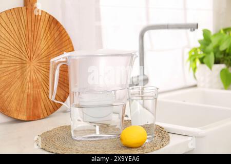 Water filter jug, glass and lemon on countertop in kitchen Stock Photo