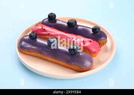 Delicious eclairs covered with glaze on light blue background Stock Photo