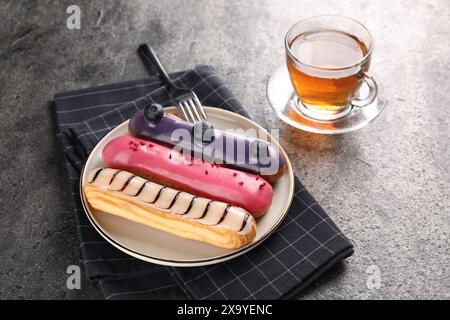 Different tasty glazed eclairs served with tea on grey textured table Stock Photo