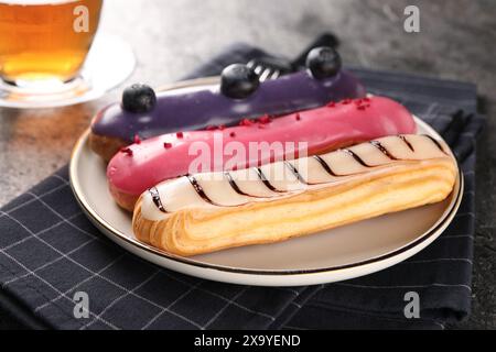 Plate with different tasty glazed eclairs on table, closeup Stock Photo