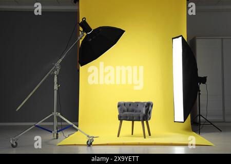 Yellow photo background, armchair and professional lighting equipment in modern studio Stock Photo