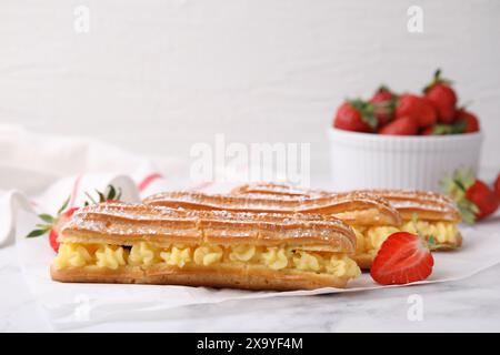 Delicious eclairs filled with cream and strawberries on white marble table Stock Photo