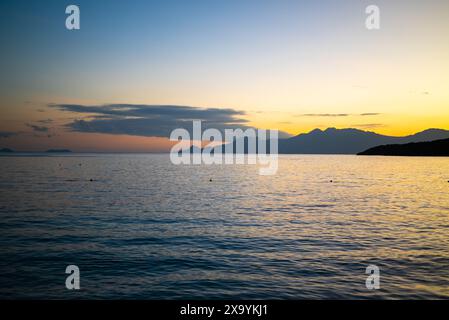 Sun setting over tranquil sea and mountains Stock Photo