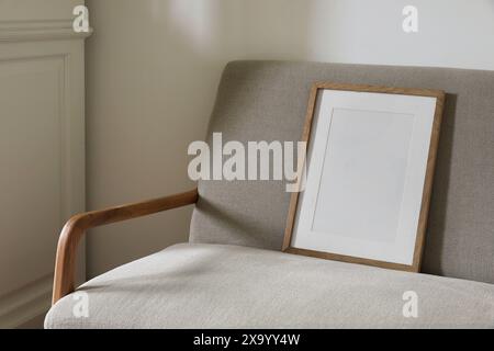 Closeup of blank wooden picture frame, poster mockup, midcentury linen sofa in sunlight. White wall background. Elegant minimal Scandinavian interior Stock Photo