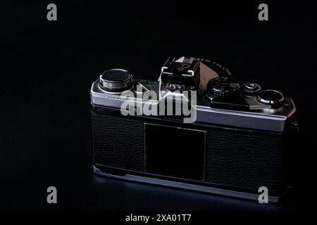 A vintage film camera with a black body and silver details, placed on a dark surface. The camera is shown from the back, highlighting its classic desi Stock Photo