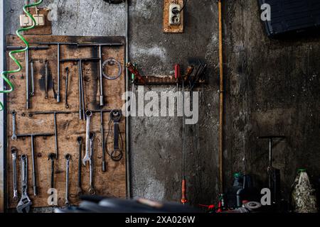 A cluttered workshop wall with various tools hanging on a wooden board and a concrete wall. Tools include wrenches, pliers, and screwdrivers. The wall Stock Photo