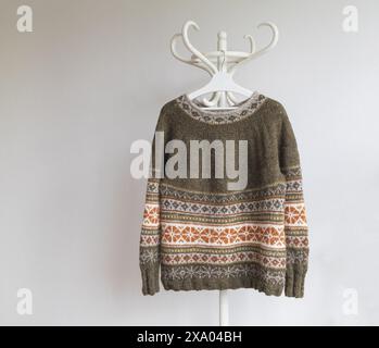 Photo of an Icelandic knitted brown wool lopapeysa sweater in traditional Nordic knitting pattern hanging on a rack against a white background Stock Photo