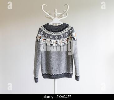 Photo of a knitted grey wool lopapeysa sweater in traditional Icelandic Puffin bird knitting pattern hanging on a rack against a white background Stock Photo