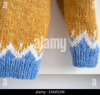 details of an Icelandic knitted wool lopapeysa sweater in traditional Nordic knitting pattern, close-up photo of yellow blue white pullover ribbed cuf Stock Photo
