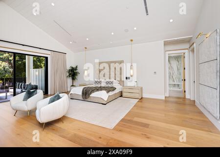 White-walled bedroom with wooden floors, featuring a bed and two armchairs Stock Photo
