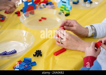 Female hands of a mother helping her child putting together the building blocks during the birthday party. Stock Photo