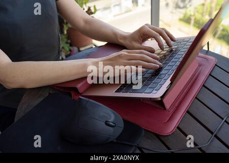 A woman works from her balcony using an ergonomic vertical mouse and a laptop stand Stock Photo