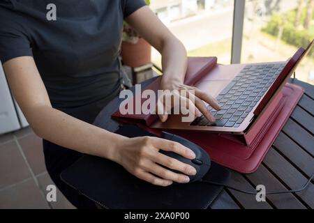 A woman works from her balcony using an ergonomic vertical mouse and a laptop stand Stock Photo