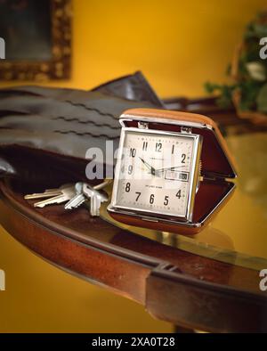 Vintage travel alarm clock with leather case beside keys on wooden table, warm indoor lighting, nostalgic still life suggesting time, routine, and tra Stock Photo