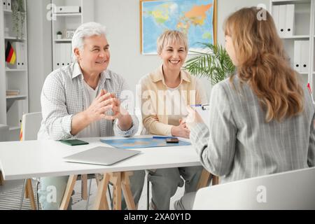 Mature couple with travel agent sitting at table in office Stock Photo