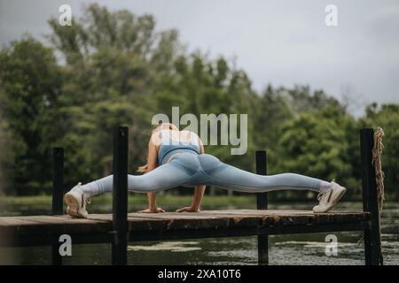Woman performing leg stretching exercise on wooden pier in outdoor park setting Stock Photo