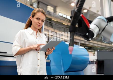 Young female entrepreneur controls robotic arm in startup factory using wireless technology. Stock Photo