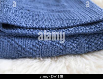 Close-up photography of an edge of a navy blue knitted blanket in brocade knitting pattern on a white lambskin fur Stock Photo
