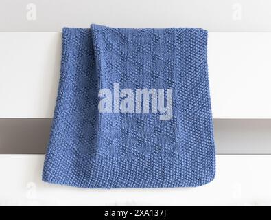 a photo of a navy blue knitted blanket in brocade knitting pattern in a white interior Stock Photo