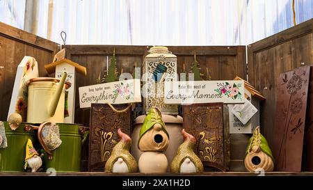 A wooden shelf with metal watering cans, cute gnome ornaments and signs with sayings on them and a bird house.  All for sale at a garden market. Stock Photo