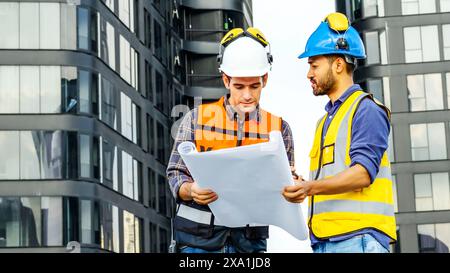 Two construction workers in protective helmets, reviewing plans near a building Stock Photo