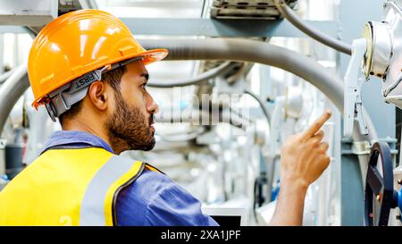 A man wearing an orange helmet pointing at metal pipes. Stock Photo