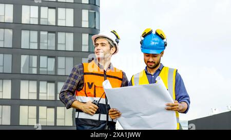 The two men reviewing blueprints for construction materials on a rooftop. Stock Photo