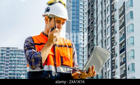 Worker in safety gear with laptop and walkie-talkie on construction site Stock Photo