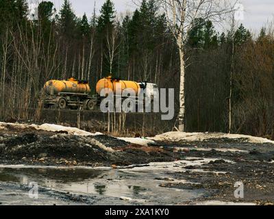 A trailer with a bright orange gas tank rides through a forest on a road in the middle of nowhere in Urals, Russia Stock Photo