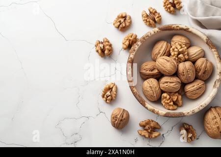 A bowl of walnuts is on a white background. The walnuts are scattered around the bowl, with some of them in the bowl and others on the table Stock Photo
