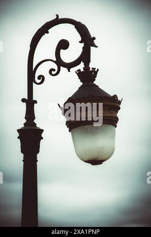 A close-up of an iron lamp post with a lit light bulb. Stock Photo