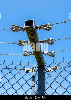 Security fence closeup of barbed wire connectors and metal post blue sky Stock Photo