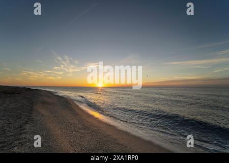 A tranquil sea beneath a golden sky at dawn. Contemplation against the backdrop of the ocean and sky. Stock Photo