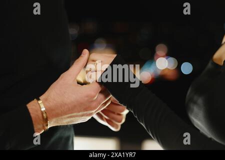 The man and woman holding hands in a night setting. The woman is wearing a gold ring Stock Photo