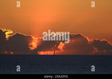 A sailboat silhouetted in the distance at dramatic sunset over the sea Stock Photo