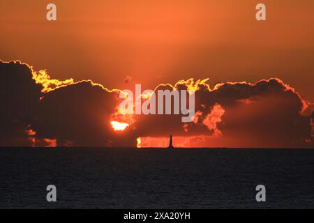 A sailboat silhouetted in the distance at dramatic sunset over the sea Stock Photo
