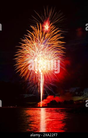 Vibrant fireworks reflecting on water at nighttime event Stock Photo
