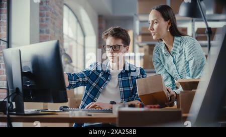 Two Employees Preparing Orders Made from Online Sales in Their Internet Shop. Man and Female Working in a Storeroom. Young Man Using Desktop Computer, Woman Confirming Contact Details on Boxes. Stock Photo