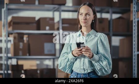 Portrait of an Inventory Manager Using Smartphone, Connecting with Colleagues, Supporting Clients Over Internet. Young Small Business Owner Working in Online Store Warehouse. Stock Photo