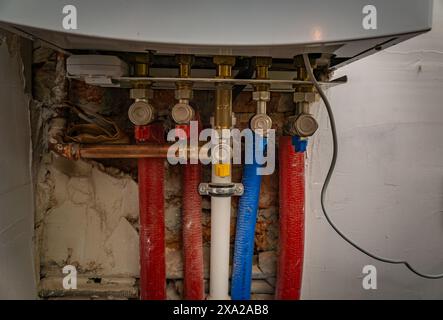 A close-up shot of plumbing pipes and valves connected to a white water heater. Stock Photo