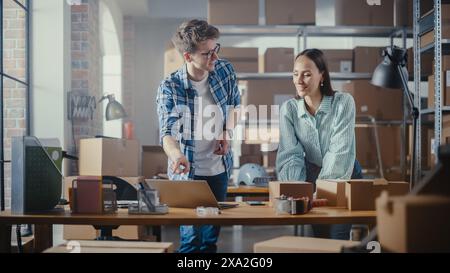 Two Successful Small Business Owners Working in Warehouse. Talking, Using Laptop Computer, Checking Retail Stock, Preparing Shipment. Sales Specialist and Inventory Manager High Five Each Other. Stock Photo