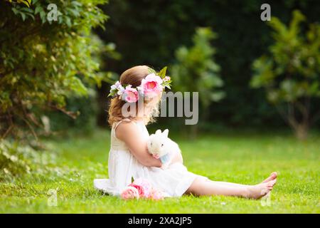 Little girl bunny in sunny garden. Summer blooming park. Child holding rabbit at Easter celebration. Egg hunt. Stock Photo