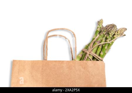 A bundle of fresh green asparagus stalks is neatly arranged in a brown paper bag, prominently displayed against a white background. Stock Photo