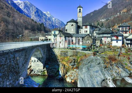 Beautiful Alpine Rustic Village with Snowcapped Mountain and a Bridge over a River in a Sunny Day in Valle Verzasca in Lavertezzo, Ticino, Switzerland Stock Photo