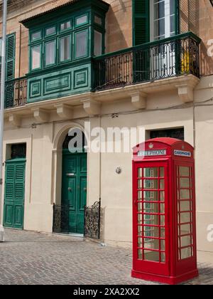 Red telephone box in front of a building with green shutters and decorative balconies, Valetta, Malta Stock Photo