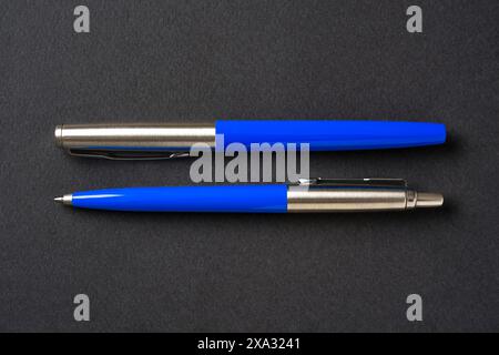 Blue plastic and metal ballpoint pen and fountain pen on dark gray isolated background Stock Photo